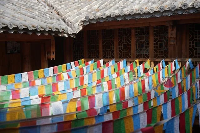 Rows of multicoloured prayer flags stretch across a courtyard beneath tiled roofs.