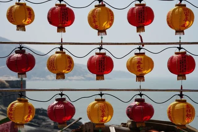 Rows of red and yellow lanterns hang against a hazy view of the coast.