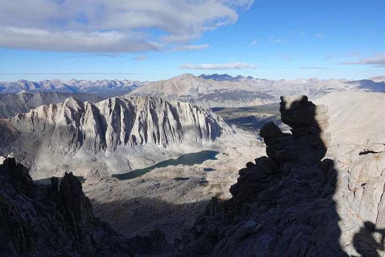 A long alpine lake appears between jagged foreground towers and the pale cliff wall beyond.