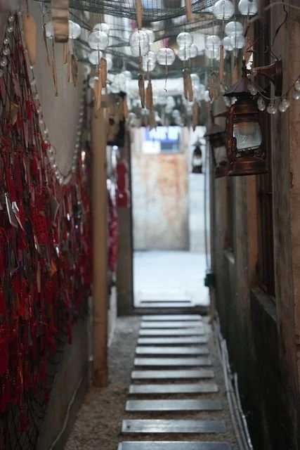 Glass wind chimes and red tags line a narrow passage, with stepping stones leading toward the light.