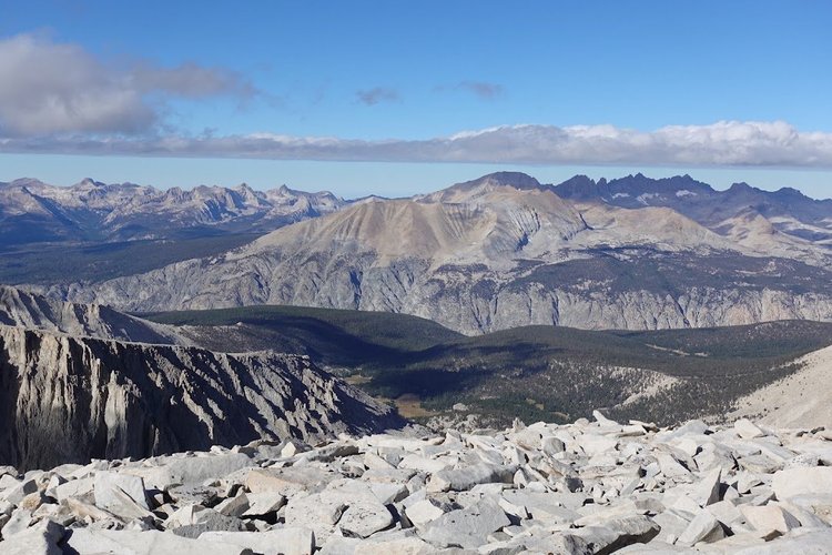 Dark forests fill the valleys beneath pale Sierra Nevada ridges, seen across a foreground of granite slabs.