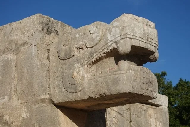 The open jaws and curved eye of a carved serpent stand out against the blue sky at Chichén Itzá.