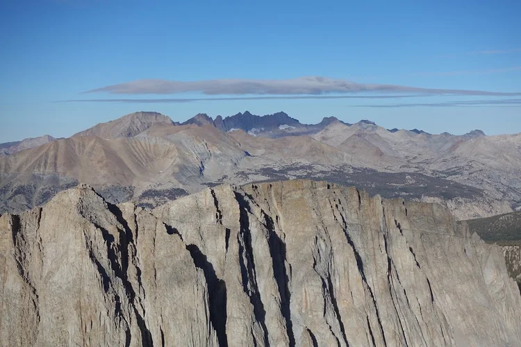 Deeply cleft cliffs frame distant Sierra Nevada ridges, with dark bands of forest in the basins between.