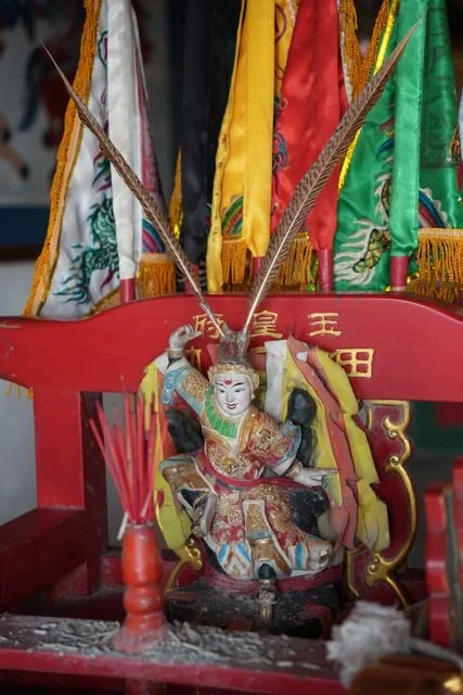 Embroidered flags and long feathers frame a painted figure on a small altar.