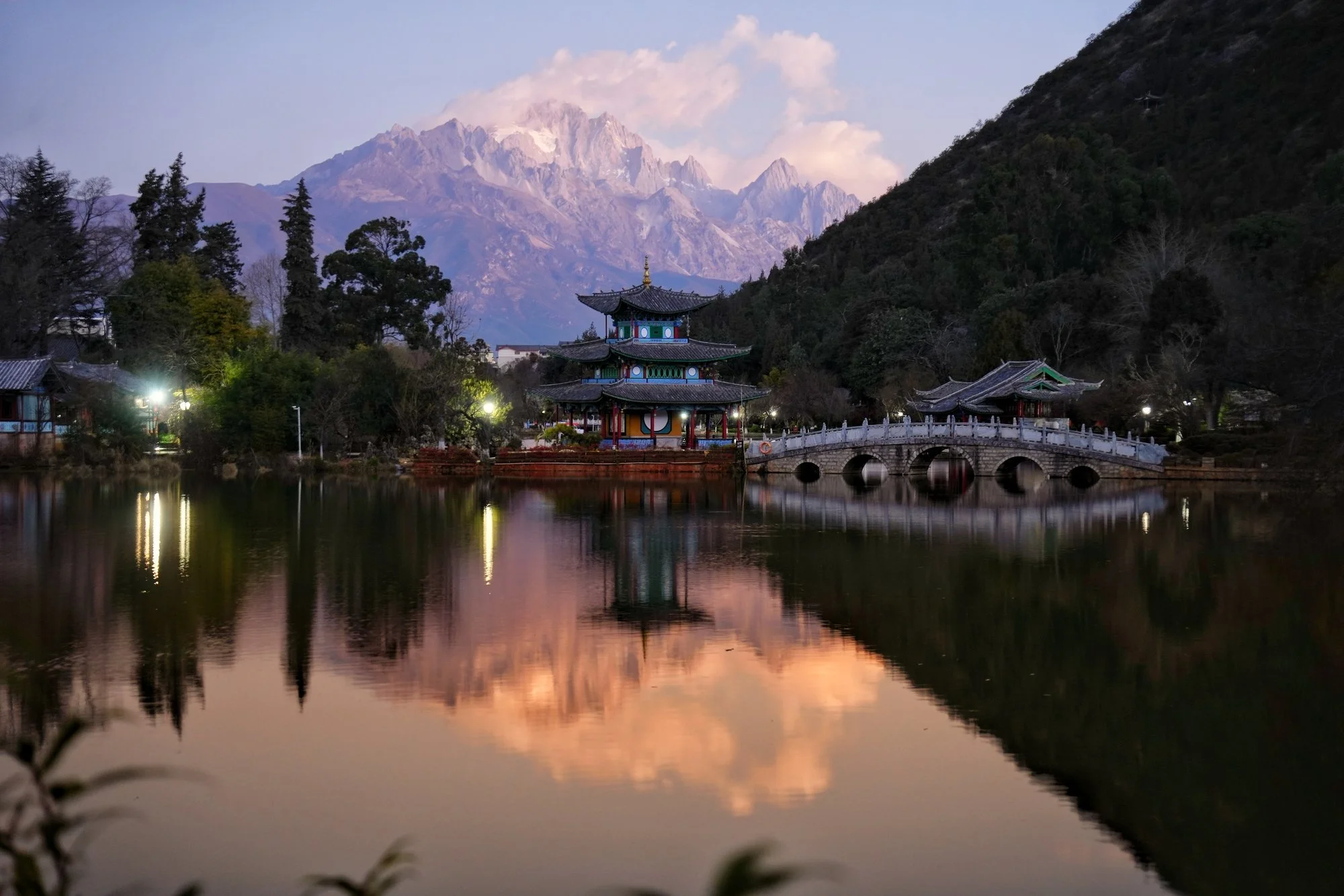 Sunrise colours Yulong (Jade Dragon) Snow Mountain above the still water of Black Dragon Pool.