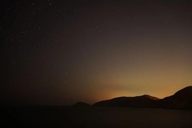 Stars fill the dark sky above the silhouetted coast.