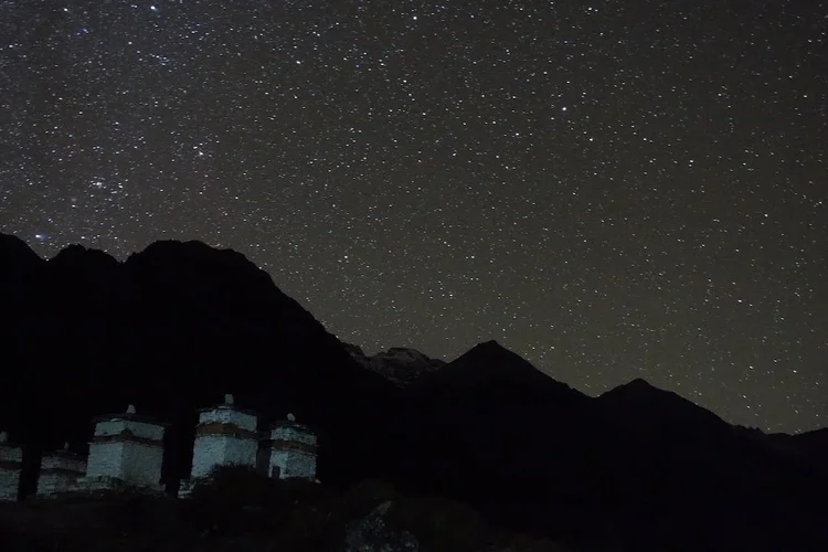 Stars fill the sky above the dark ridgeline and the pale outlines of the chortens.