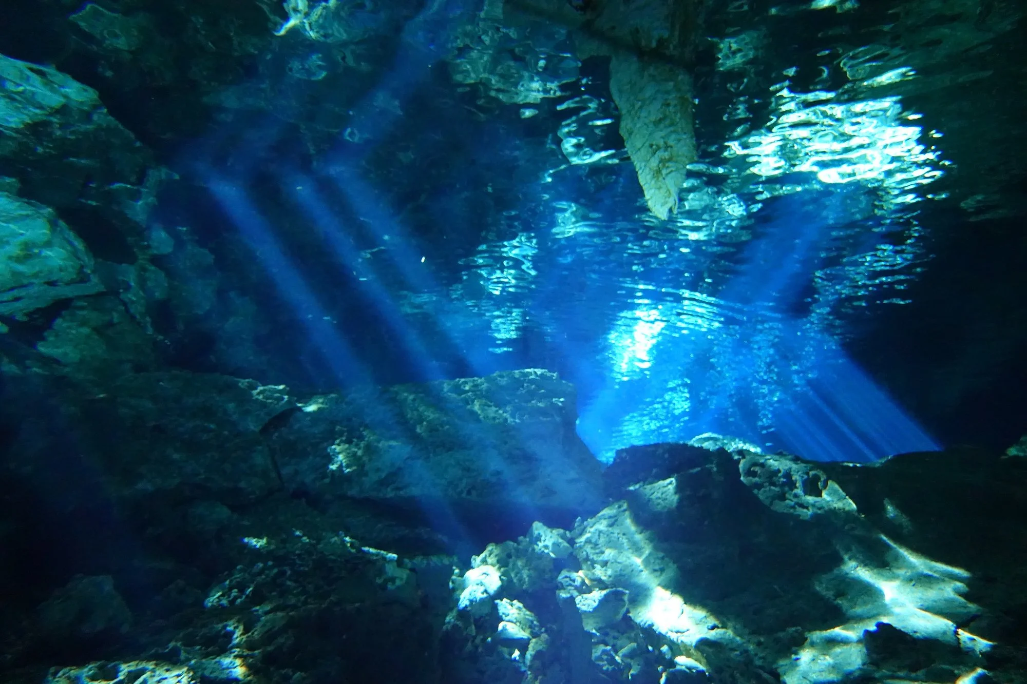 Shafts of sunlight illuminate submerged rock beneath the rippled surface.