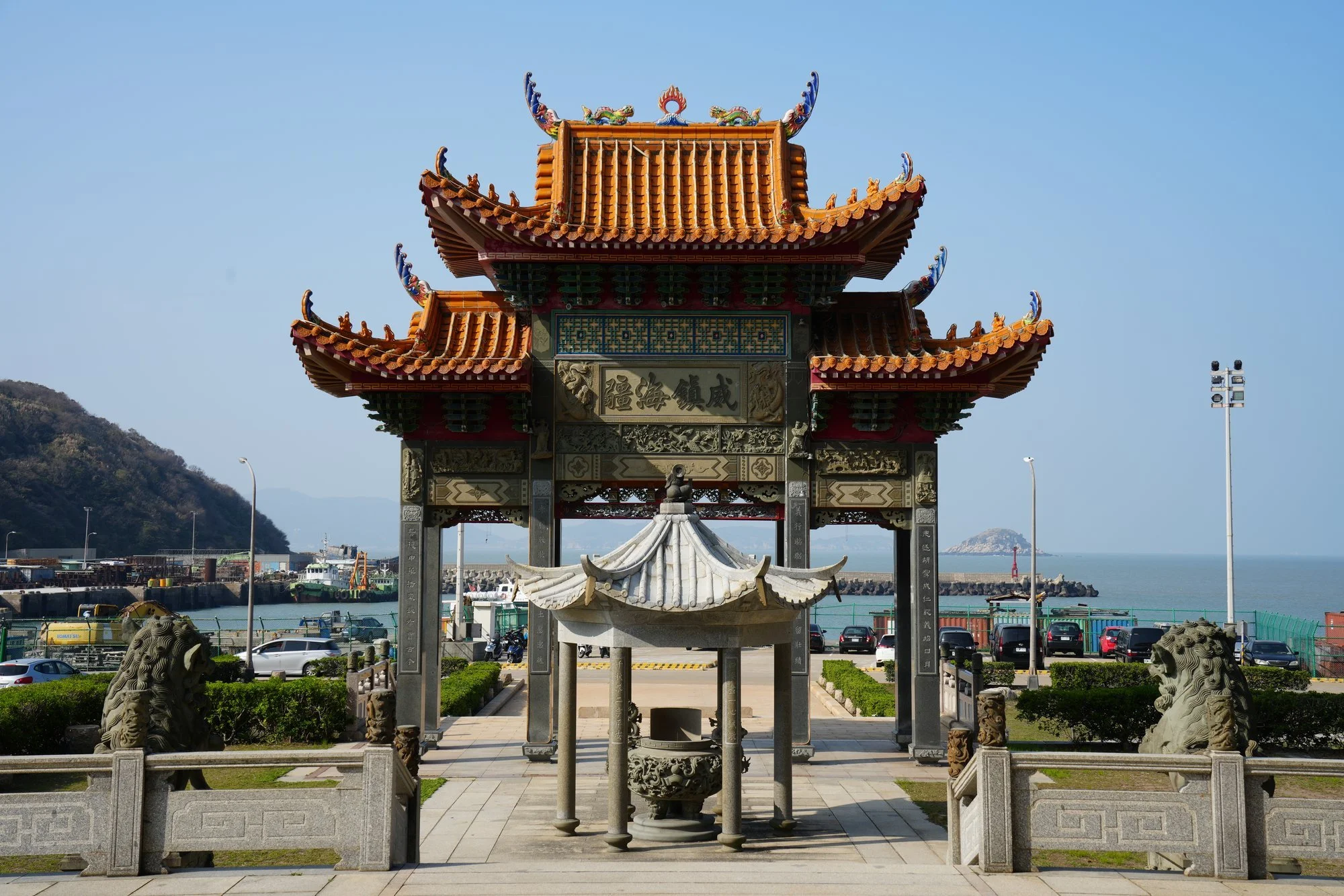 Curved orange roofs and carved stonework frame a temple gateway above the harbor.