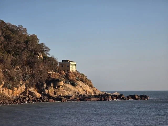 Late light falls on a weathered house and a small concrete lookout on Beigan's rocky shore.