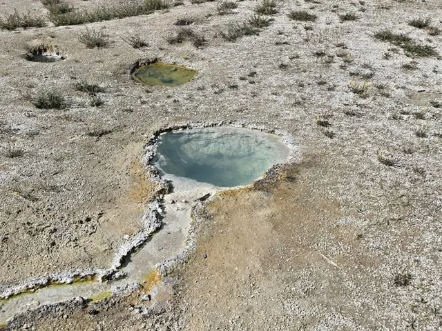 Three small pools punctuate the pale mineral surface at West Thumb.