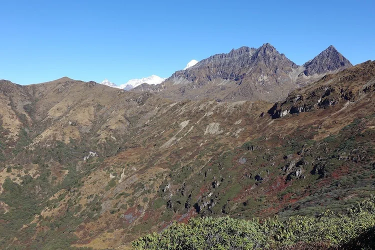 Snowy summits peek over the brown ridges, while green shrubs fill the foreground on the final day's route.