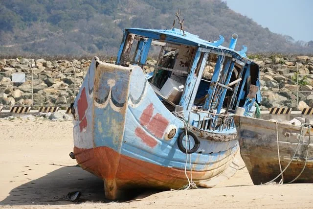 Blue paint peels from the wooden bow and cabin of a boat resting on the sand.