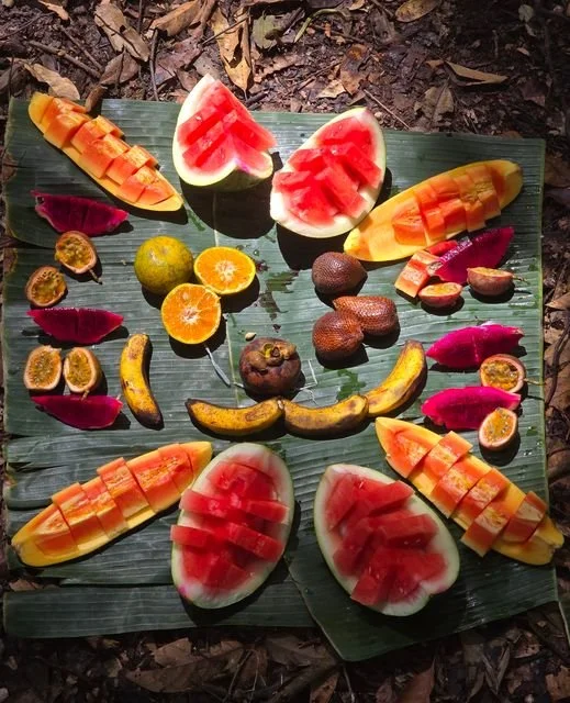 Watermelon, papaya, dragon fruit and other fresh fruit are arranged on leaves for a trail-side break.