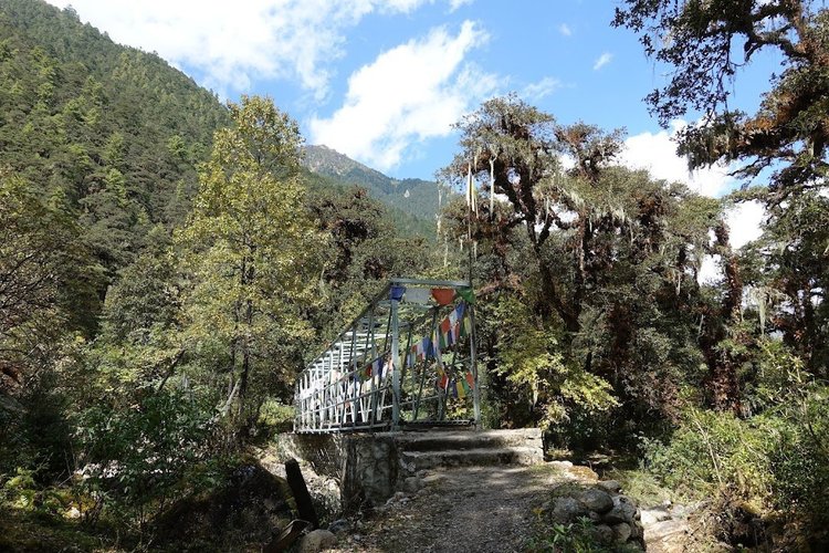 Prayer flags line a steel footbridge over the river.