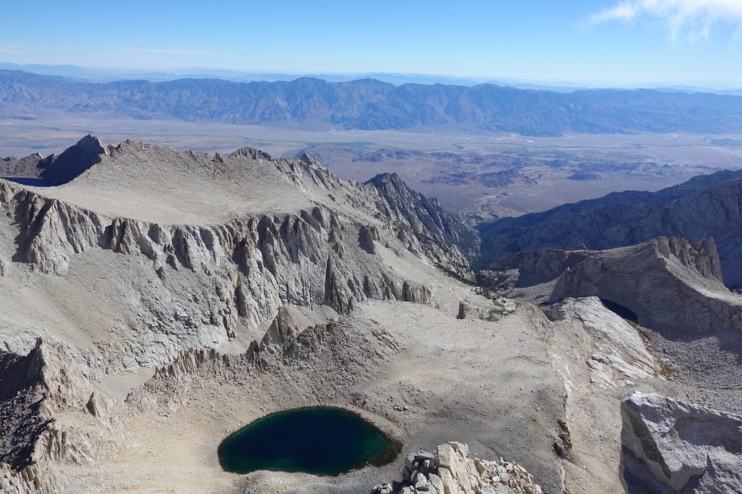 A deep blue-green lake lies beneath pale granite cliffs, with the broad valley floor and distant ranges beyond.
