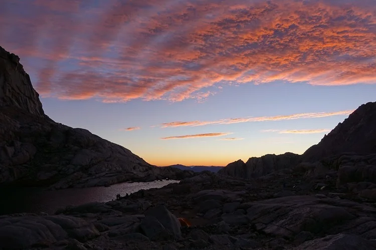 Orange dawn clouds stretch over the lake and its surrounding granite slopes.