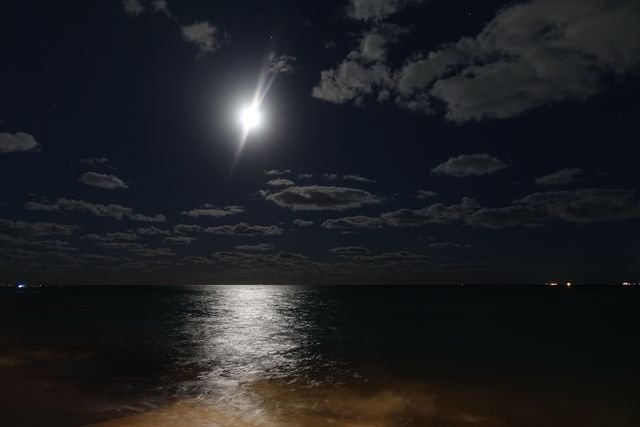 Moonlight draws a silver path across the sea beneath scattered clouds.