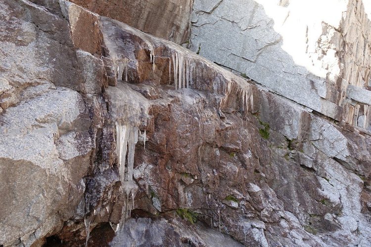 Long icicles hang from ledges in the granite, with thin sheets of ice coating the rock below.