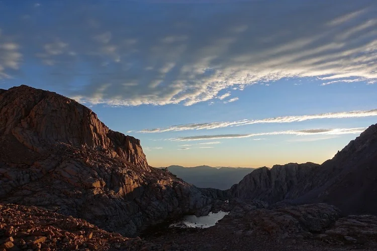 Warm light reaches the left-hand cliffs while a small lake and the rocky basin below remain in shade.
