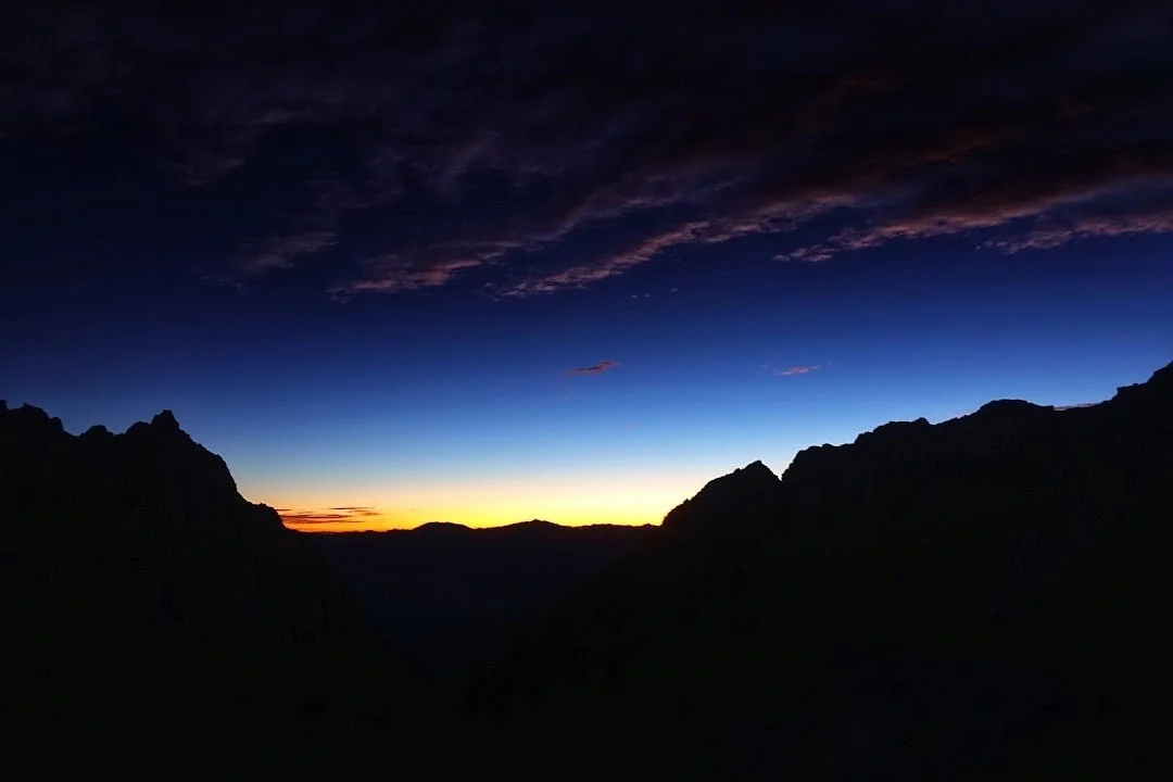 A narrow band of orange dawn glows between the dark ridges above the Mount Whitney Trail.