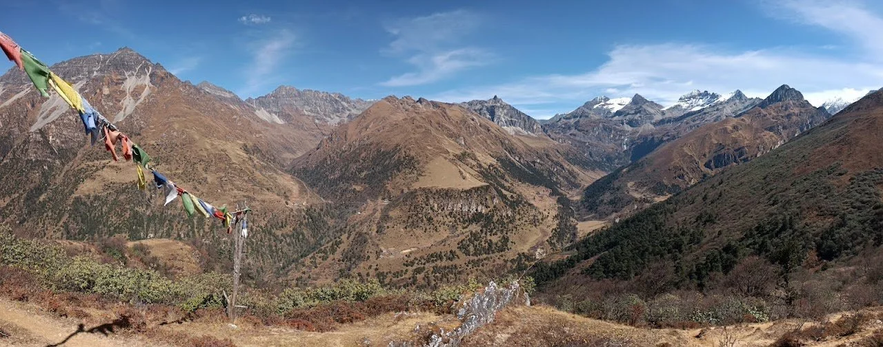 Prayer flags frame a wide view back across wooded slopes and bare mountain ridges.