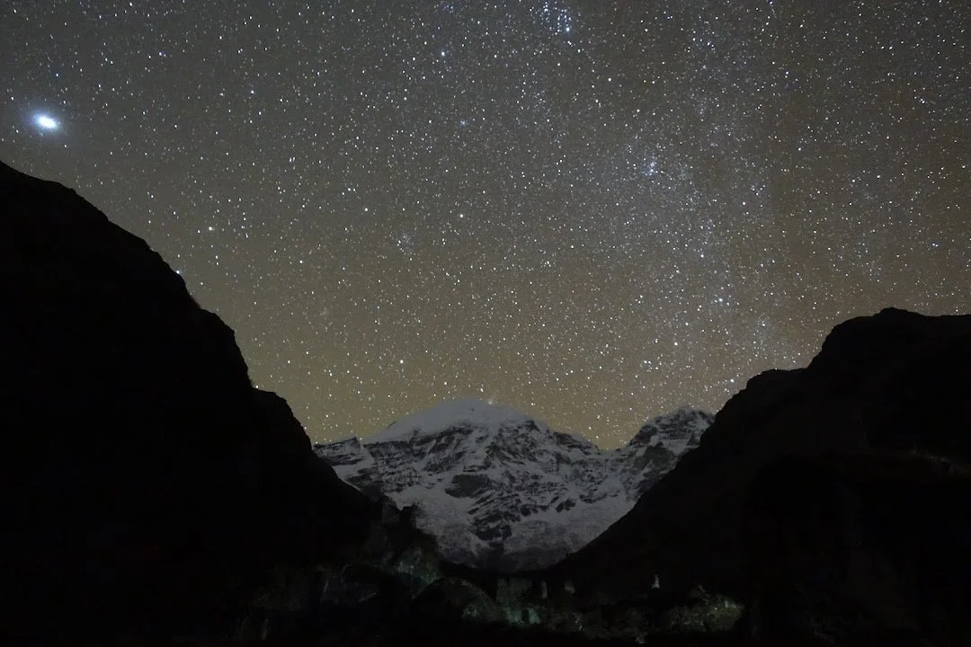 Chomolhari’s snowy face rises between dark valley walls beneath a sky crowded with stars.
