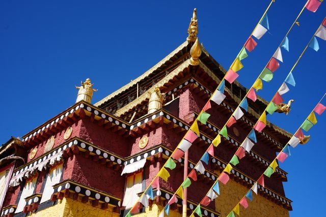 Prayer flags cross the red and yellow walls of a temple building.