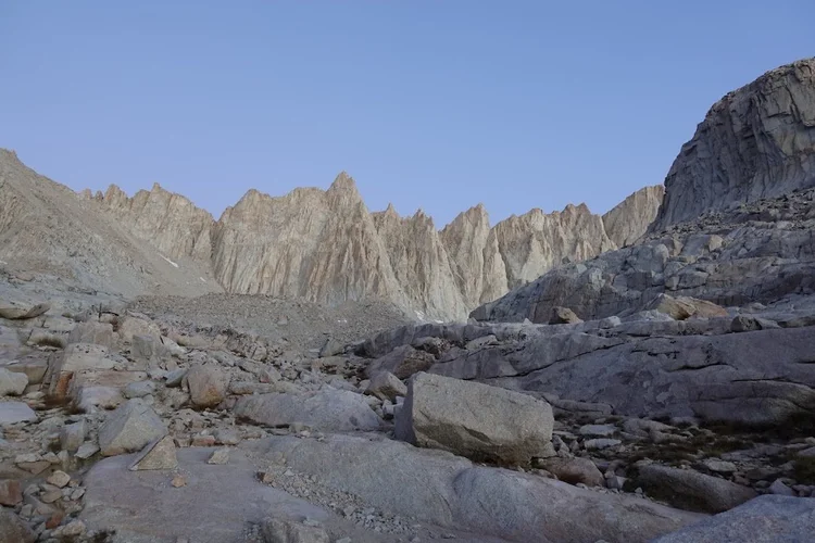 A serrated wall of granite rises above slabs and scattered boulders on the upper trail.