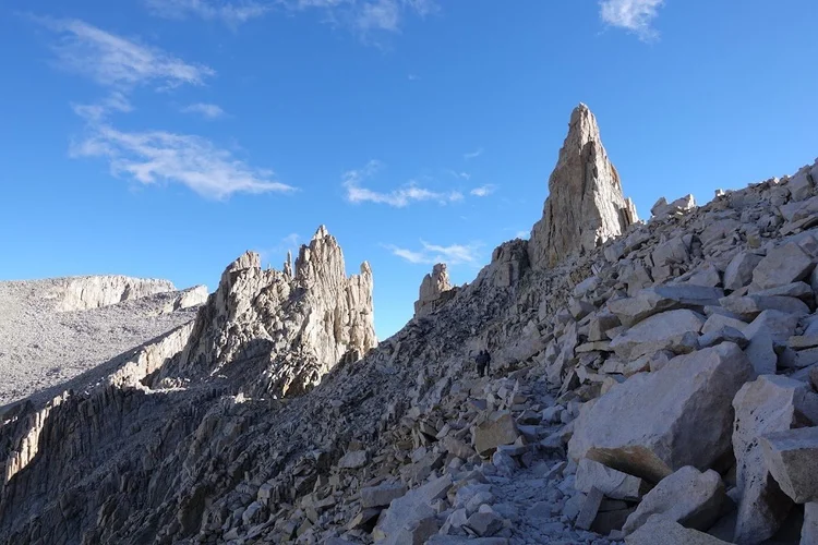 The narrow summit trail crosses a steep field of broken granite beneath sharp rock towers.