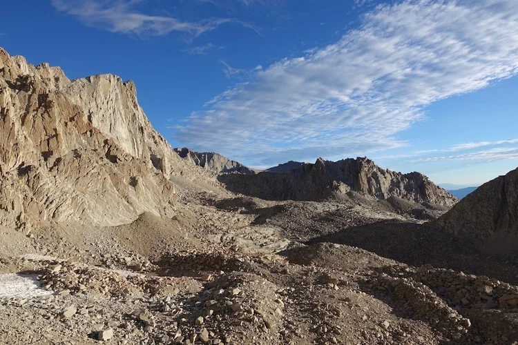 A stony trail winds through the bare upper basin, enclosed by steep granite walls and broken ridges.