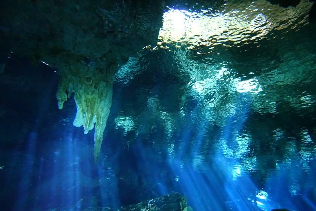 A hanging cave formation meets the rippled surface above shafts of blue light.
