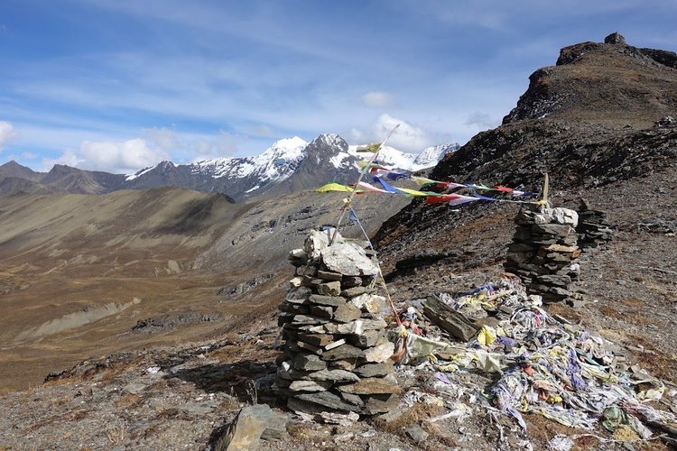 Prayer flags stretch between stone cairns at Bongteyla Pass, with snow-streaked peaks beyond.