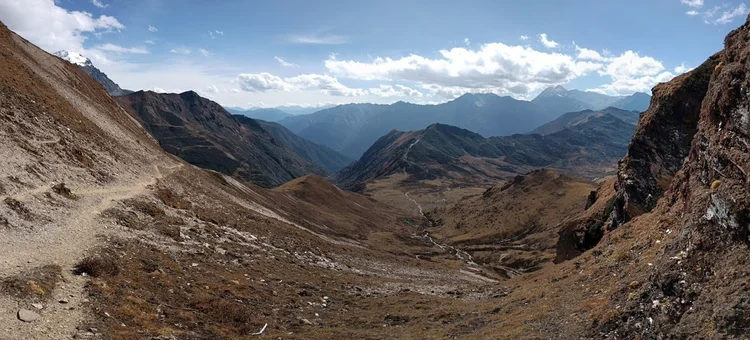 The path crosses a bare slope above a stream, with successive mountain ridges fading into the distance.