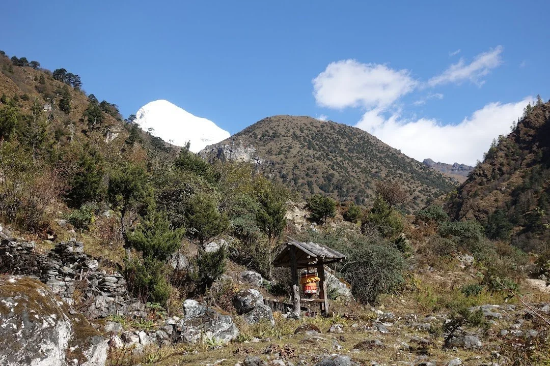 Chomolhari's snow-covered summit rises beyond a prayer wheel and the lower, scrub-covered hills.