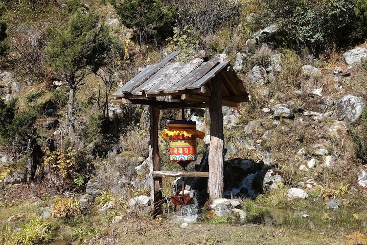 A brightly painted prayer wheel turns above a narrow stream under its timber roof.