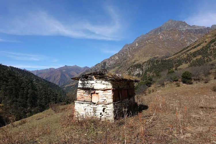 A small stone building with wooden shutters stands above the forest on the climb out of Yaktsa.