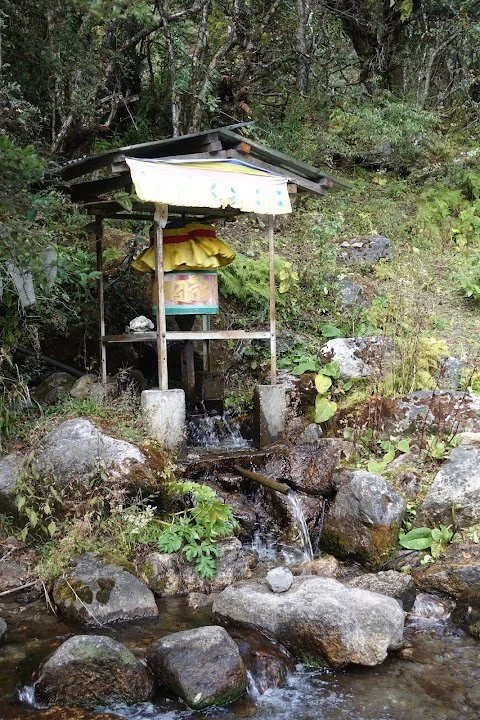 A small water-powered prayer wheel stands beneath a wooden shelter.