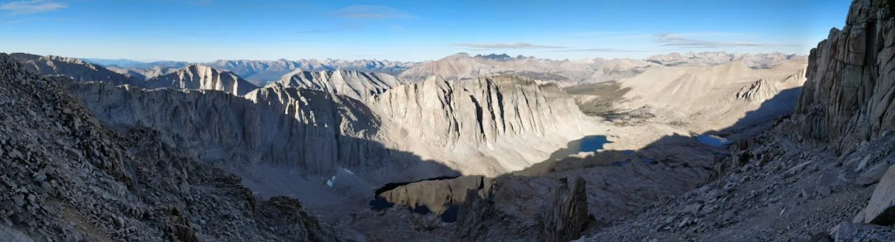 A wide view across alpine lakes, sheer granite walls and distant forested basins on the western side of the crest.