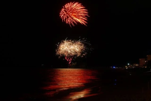 Red and gold fireworks reflect across the sea at the turn of the year.