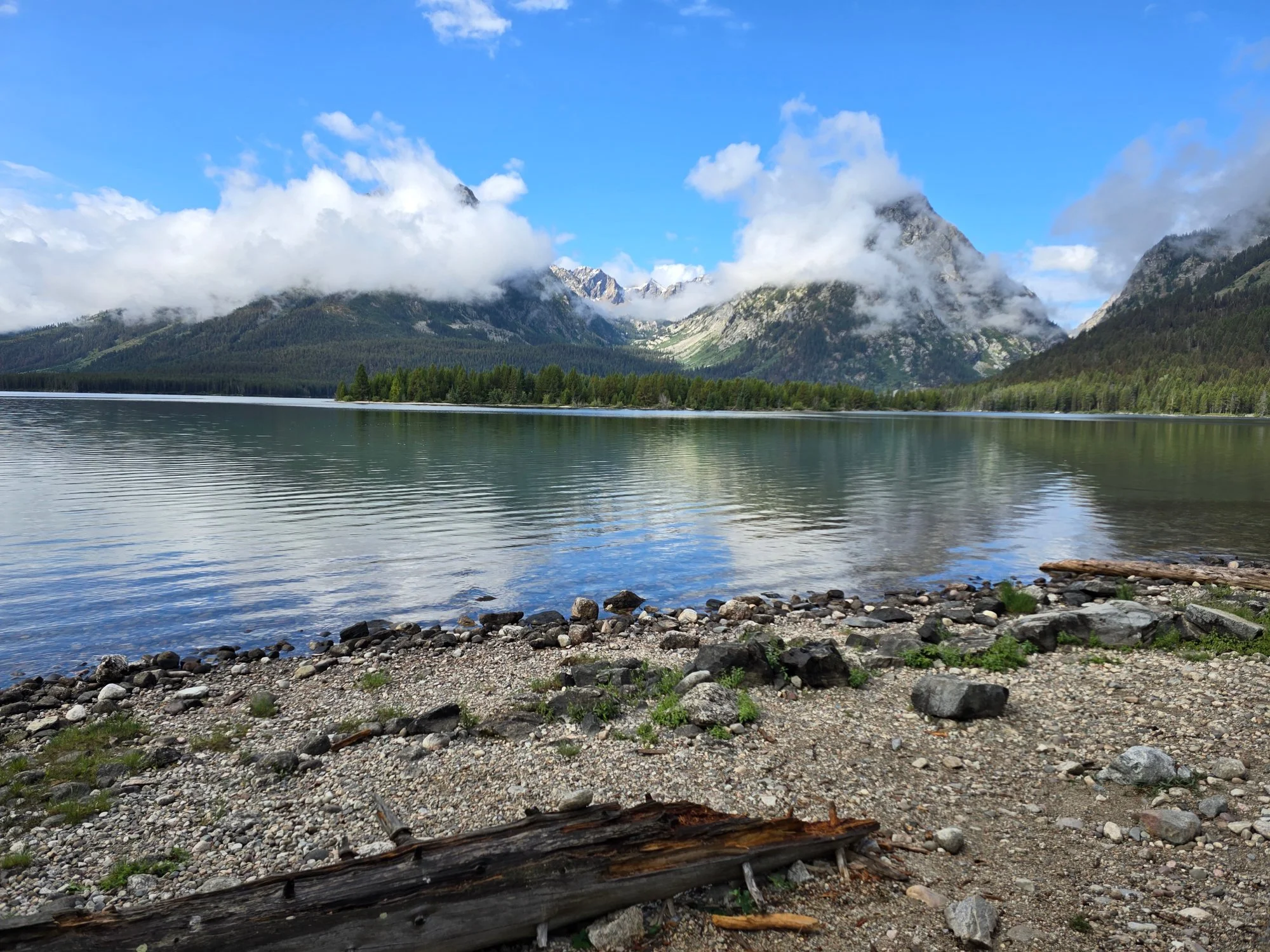 Cloud wraps the mountains above Leigh Lake, while small ripples cross the water toward a stony shore.