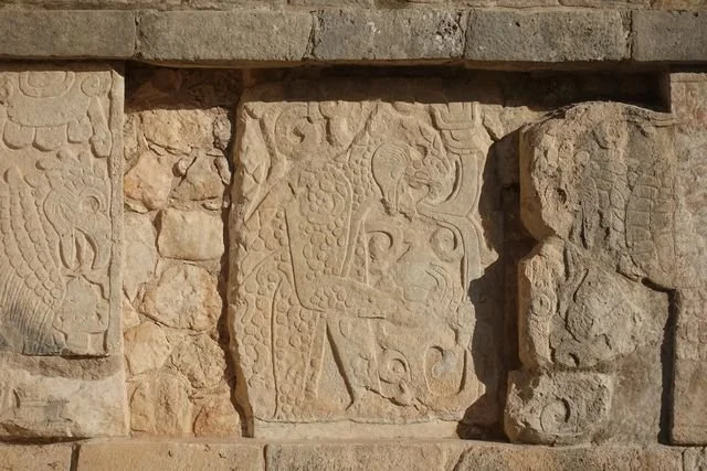 Low sunlight picks out an animal figure and curling motifs in a weathered relief at Chichén Itzá.