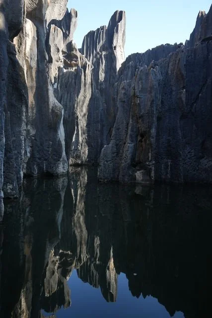 Pale stone towers and dark clefts are repeated in the water below.