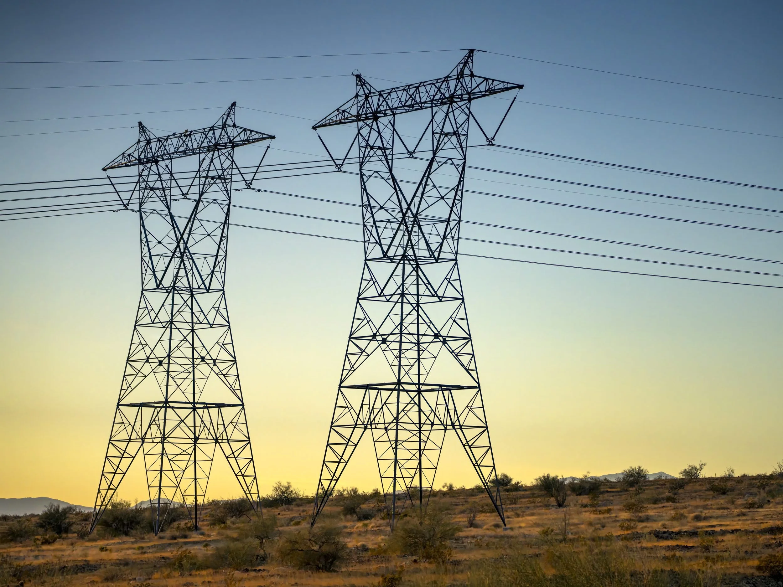 Twin high-voltage transmission towers at sunset in the desert