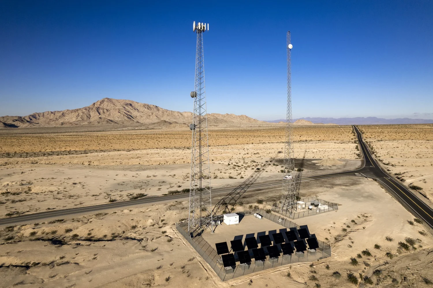 Drone aerial of communication towers powered by a solar array in the desert