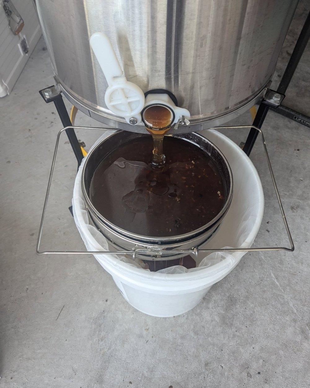Raw honey flowing from the extractor into a bucket