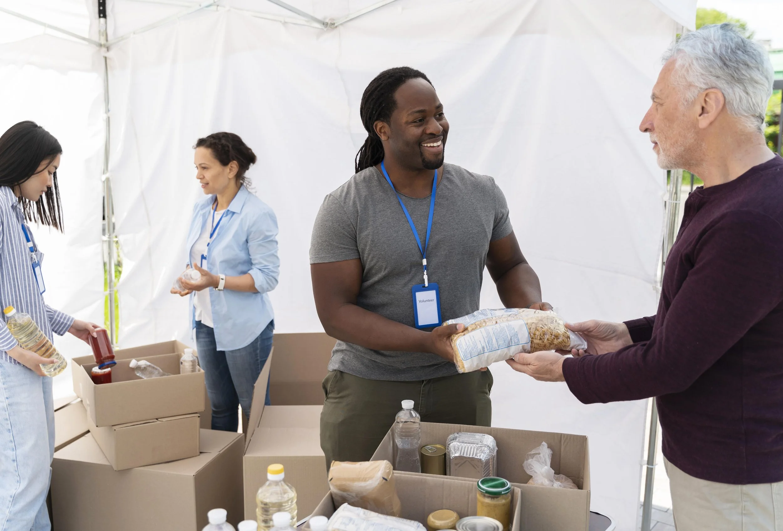 A Black man smiling and serving food to people at a food bank.
