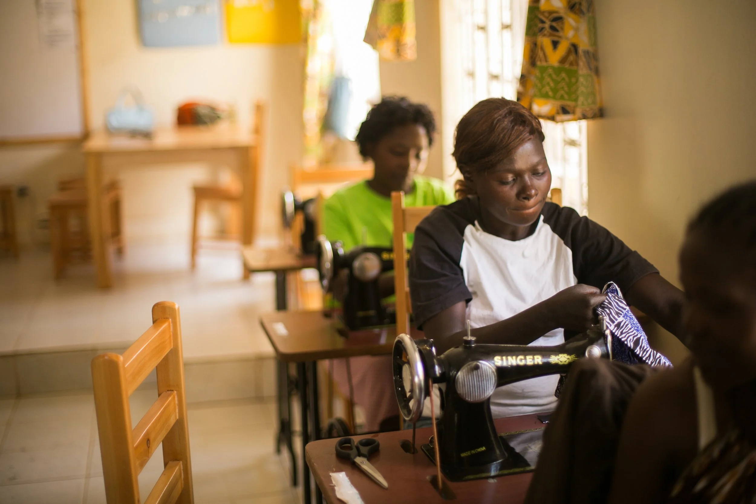 Two Kenyan women sewing with machines in a town work center.