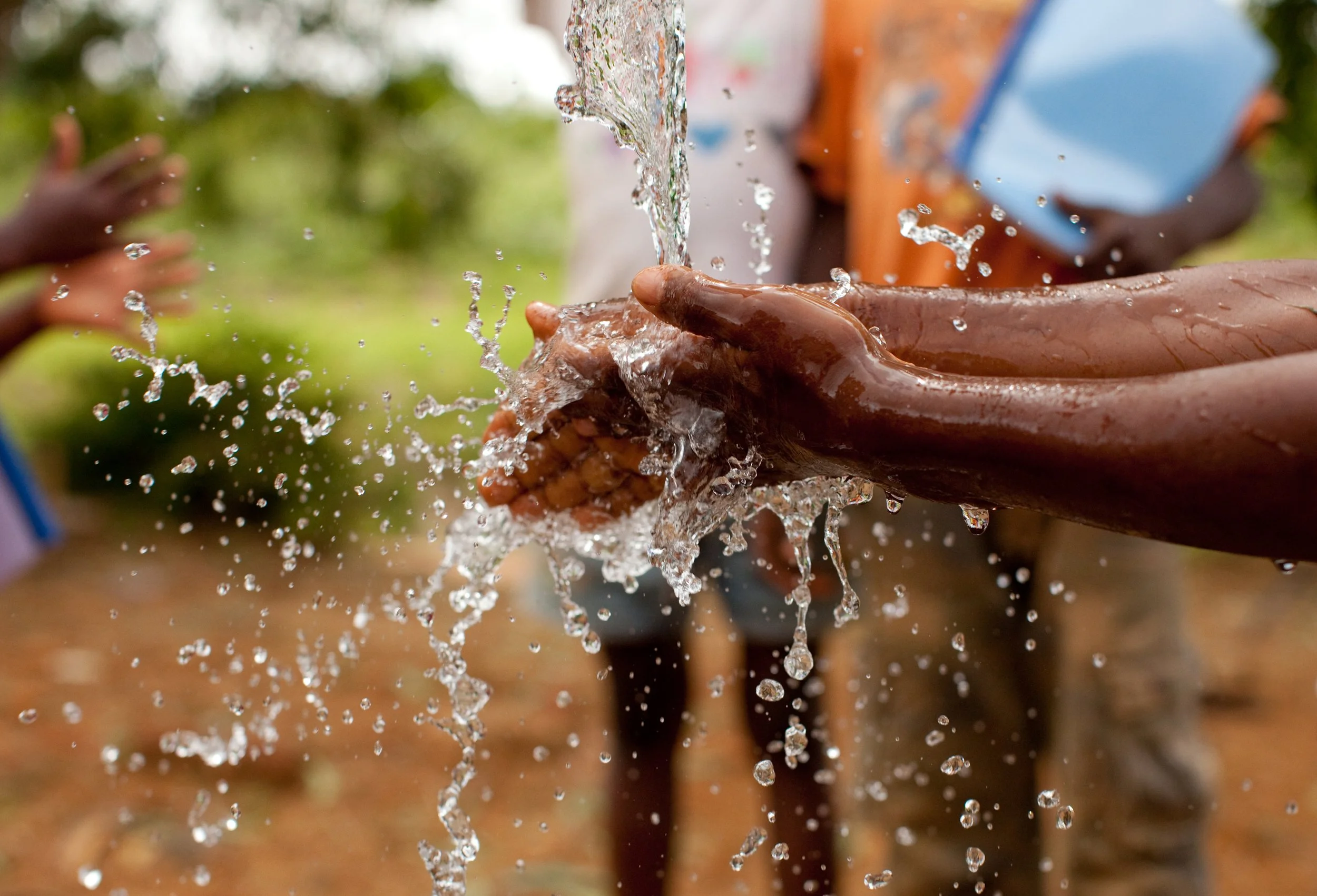Hands of a Nigerian child held under a water spout, providing clean water to a village.