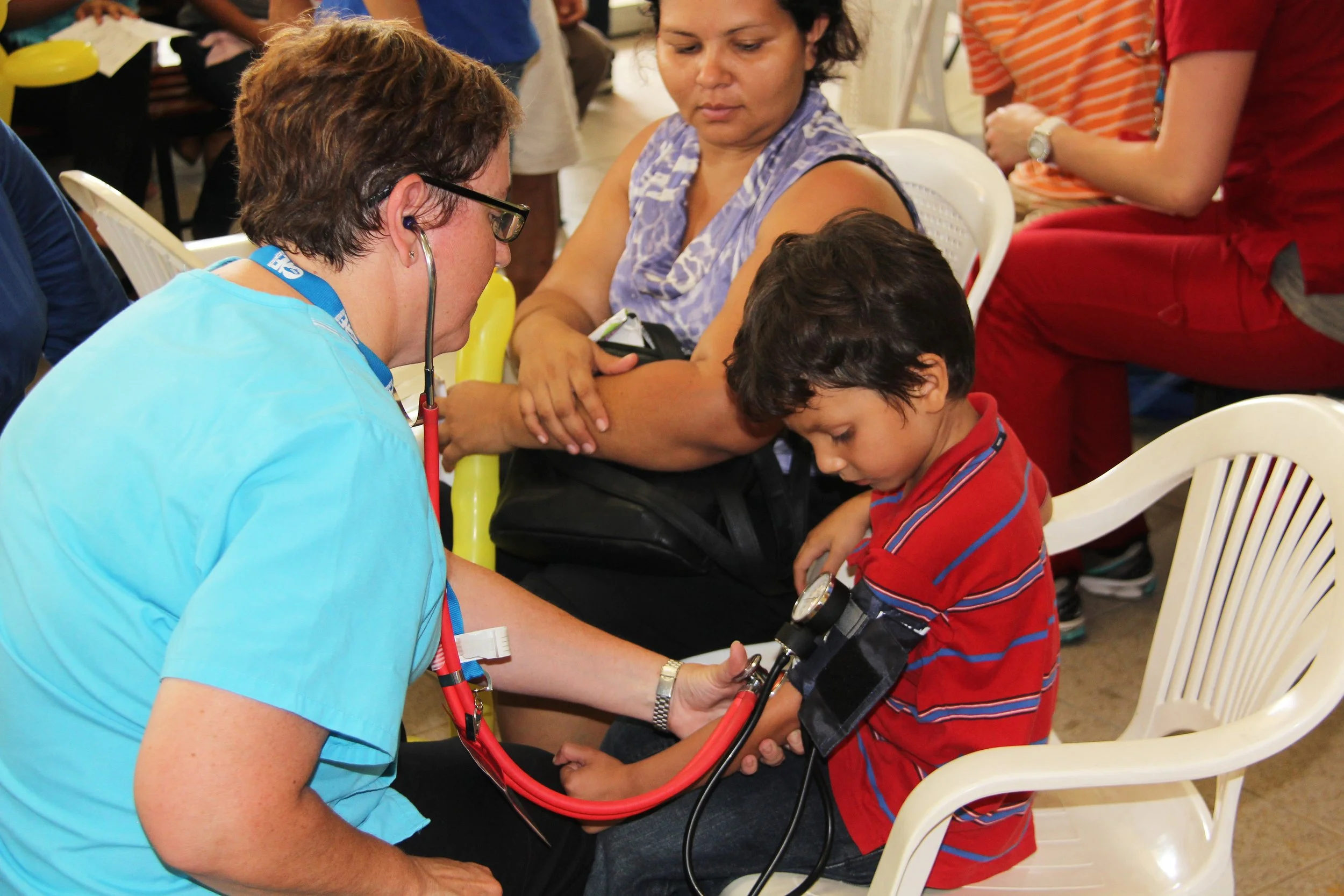 An American nurse bending down to take blood pressure of a young Guatemalan boy.